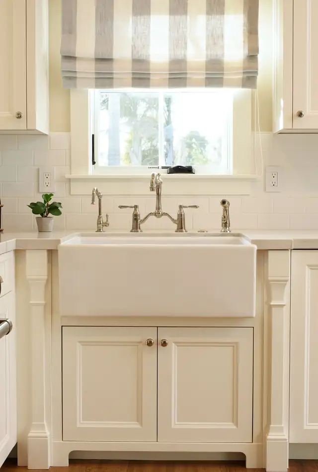 Pleasure Point coastal cottage kitchen with a white farmhouse sink, cream cabinets and a bridge faucet under a striped shade