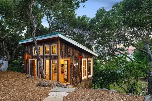 Rustic detached ADU in Santa Cruz with reclaimed wood siding, a pitched metal roof and French doors under oak trees