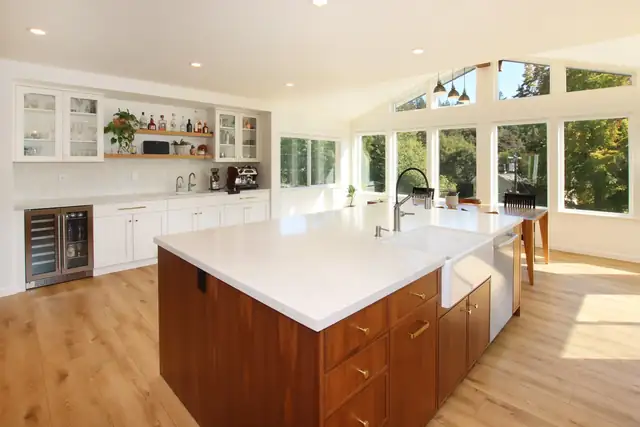 Bright kitchen with a large white quartz island on wood base cabinets, a farmhouse sink and a wall of windows